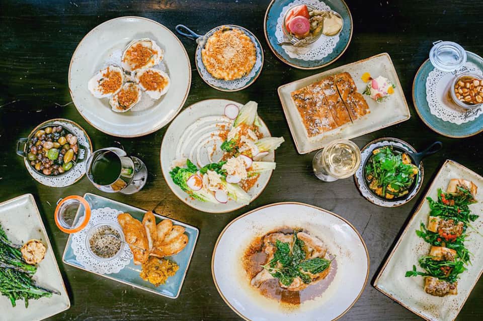 Overhead view of upscale restaurant dishes including oysters, shrimp, and gourmet appetizers on dark table