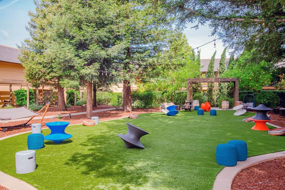 Kids play area with colorful climbing structures, artificial turf, trees, and shade elements