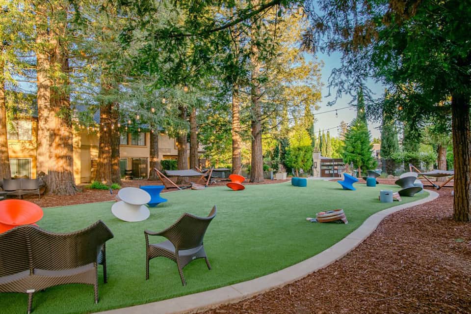 Modern resort courtyard with green synthetic turf, large trees, and colorful art sculptures
