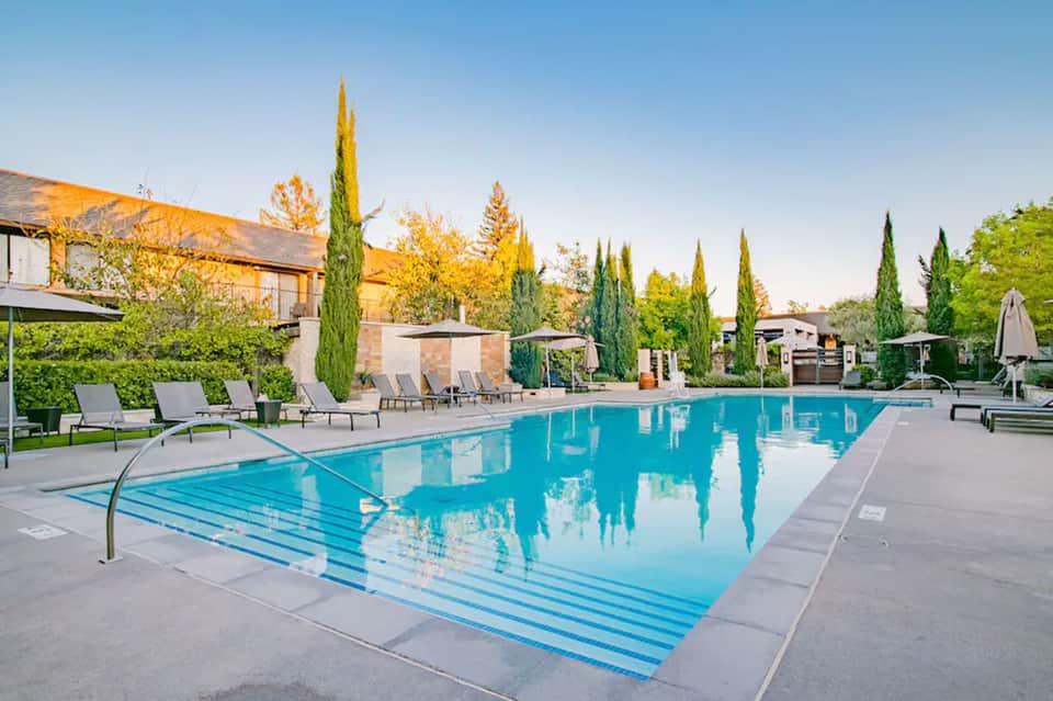 Resort lap pool with crystal-blue water, cypress trees, lounge chairs, and modern stone buildings