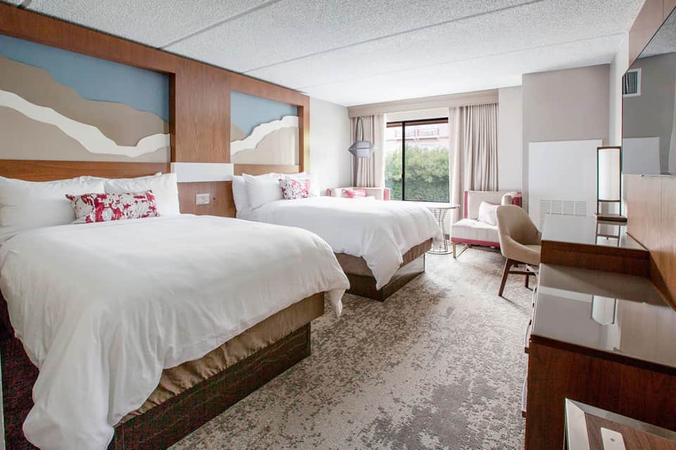 Spacious hotel room with two queen beds, wood headboards, and pink accents