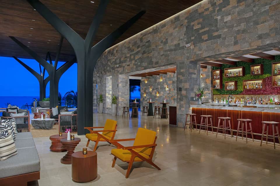 Modern resort bar and lounge with stone walls, wooden ceiling, ocean view at dusk