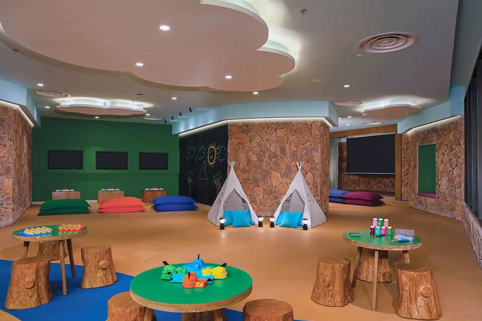Colorful children's play area with teepees, wooden furniture, green walls, and interactive activities