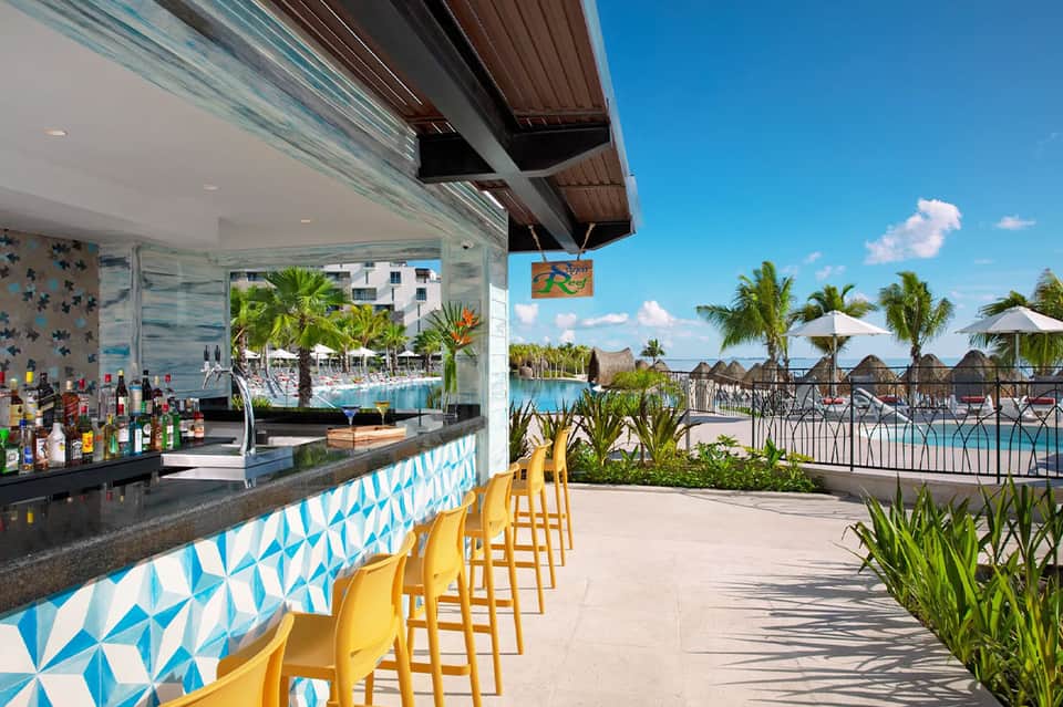 Tropical bar overlooking resort pools with yellow stools and decorative blue tile work