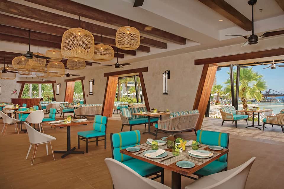 Upscale restaurant interior with woven pendant lights, turquoise cushioned seating, and ocean views