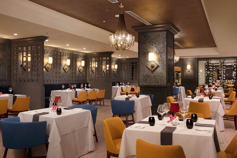 Elegant fine dining restaurant with decorative wall panels, chandeliers, and colorful chairs