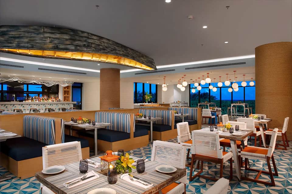 Modern hotel restaurant and bar with striped seating, pendant lights, and panoramic windows at dusk