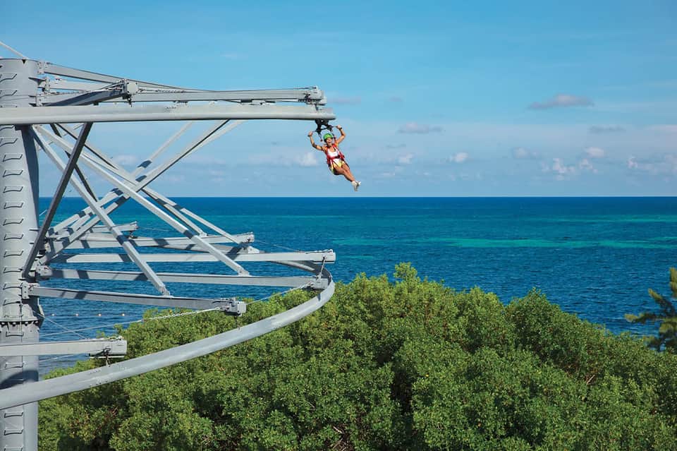 Guest ziplining over ocean on steel structure with crystal blue water and mangrove below