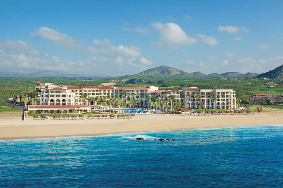 Beachfront resort building with red-tiled roof nestled against sandy beach and blue ocean