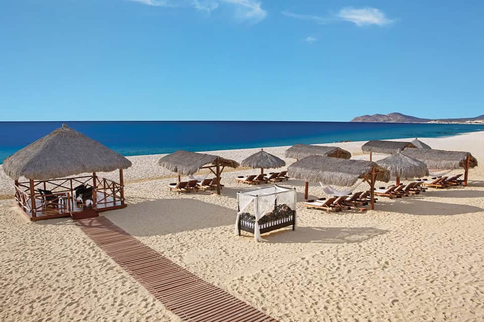 Beach club with thatched umbrellas, lounge chairs, and ocean views under clear sky