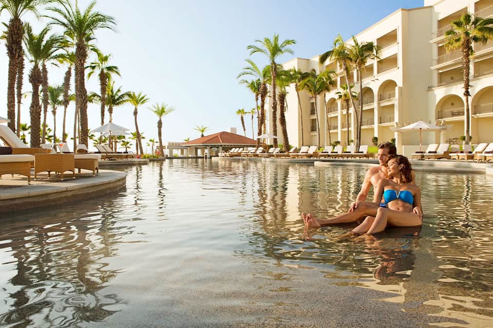 Couple wading in shallow lagoon water at beachfront resort with palm trees