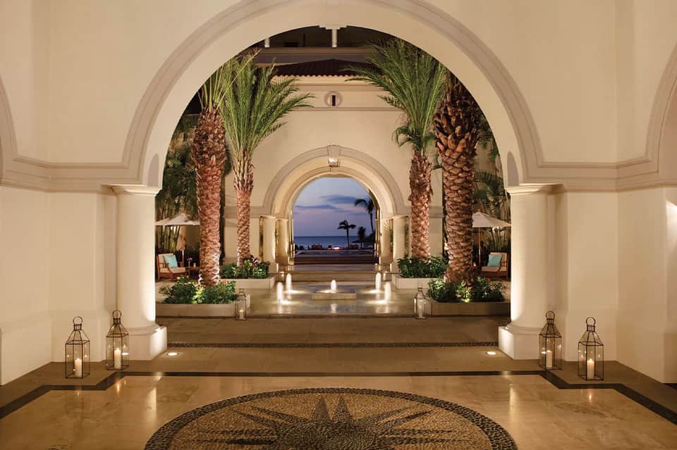 Elegant archway with palm trees leading to illuminated oceanfront promenade at dusk