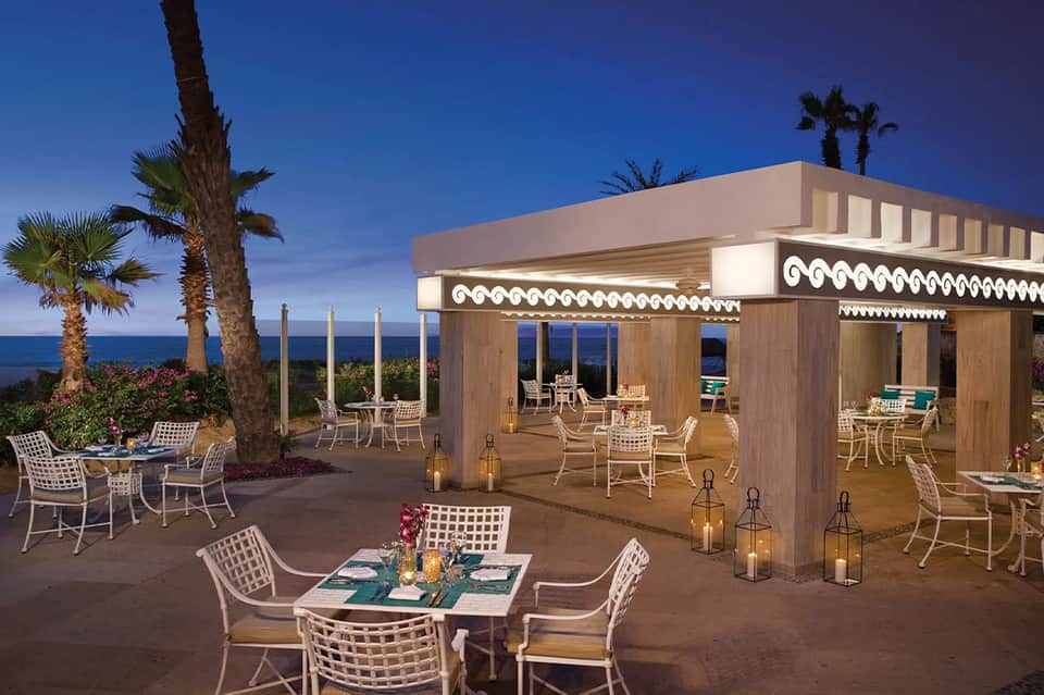 Oceanfront terrace dining area with white lounge chairs and modern wood pavilion at dusk