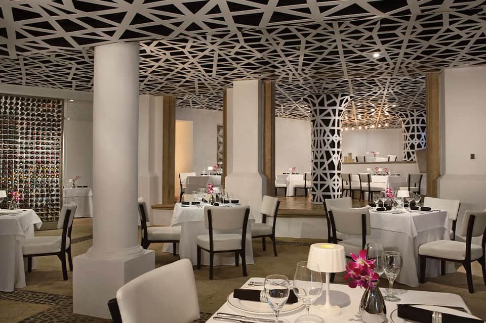 Upscale restaurant dining room with geometric patterned ceiling, white tablecloths, and elegant table settings