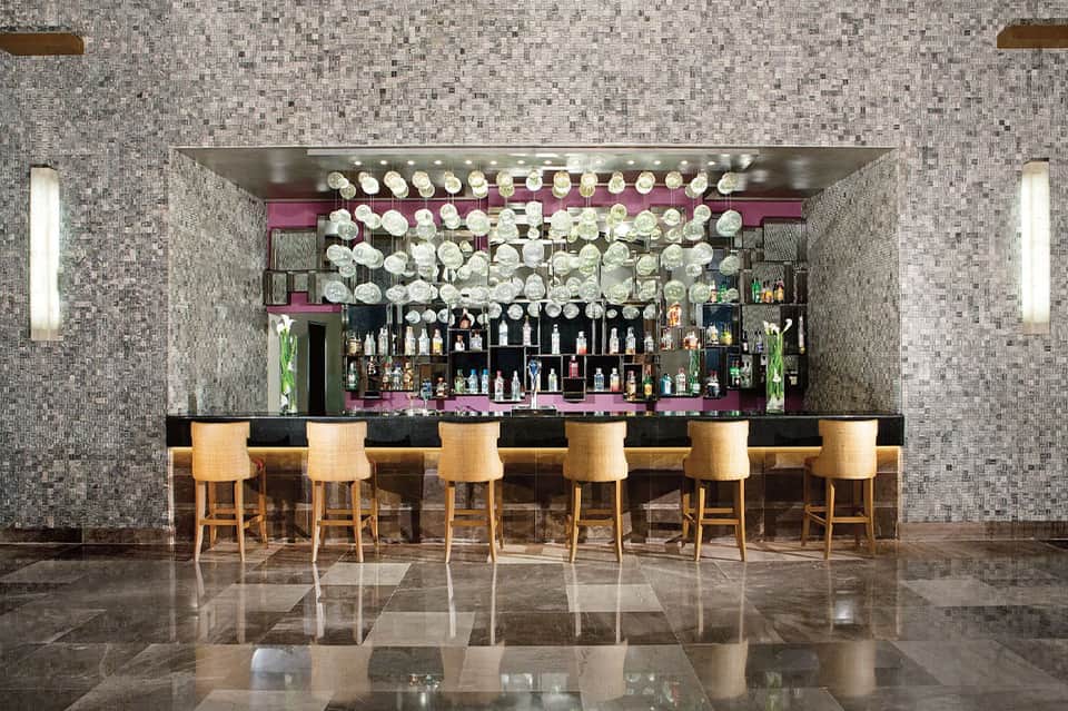 Contemporary bar with gray mosaic tile walls, illuminated disc ceiling detail, and wooden bar stools