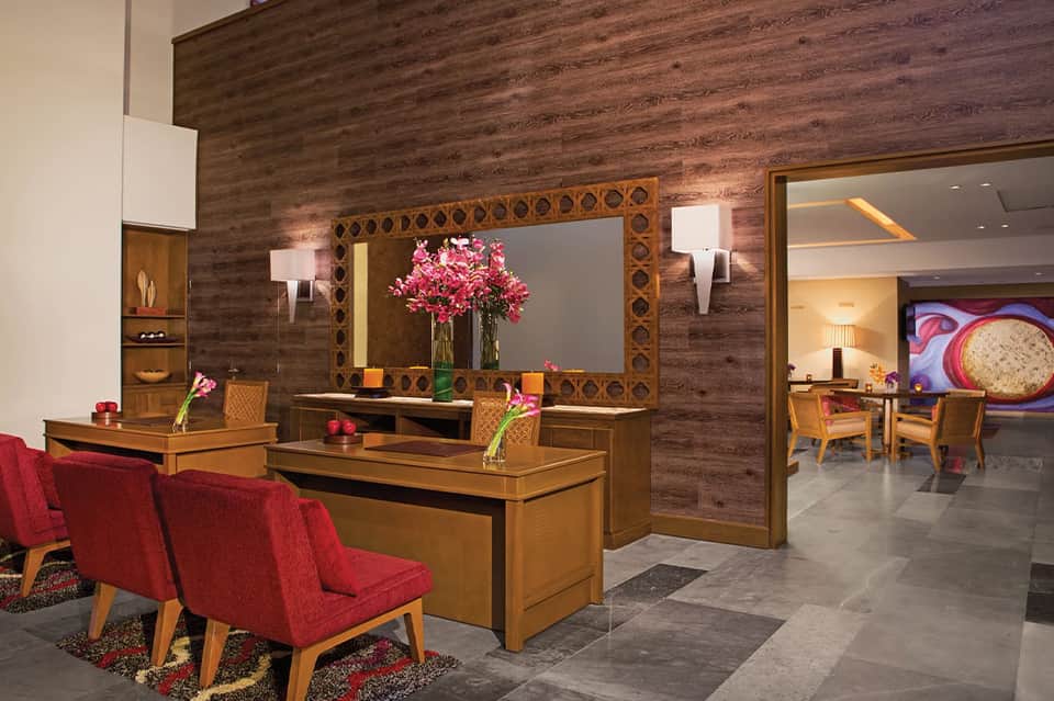 Hotel lobby with wood-paneled walls, decorative mirror, fresh flowers, and modern furnishings