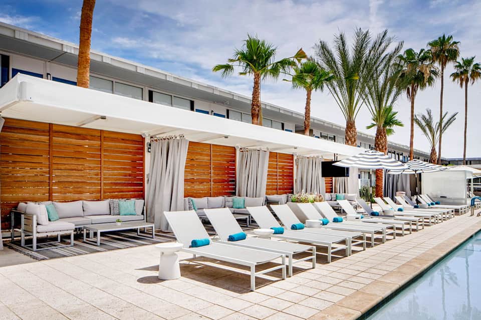 Modern poolside cabanas with white loungers, turquoise accents, and palm trees against hotel building