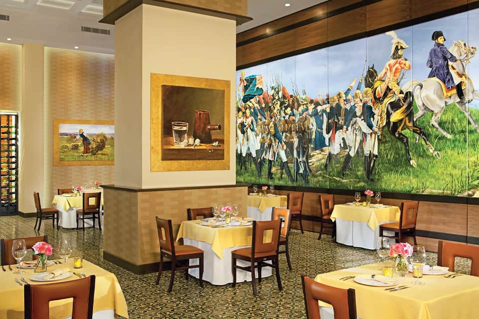 Fine dining restaurant interior with elegant yellow tablecloths and large historical cavalry artwork