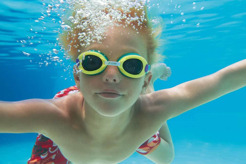 Child snorkeling underwater wearing yellow goggles in clear blue water