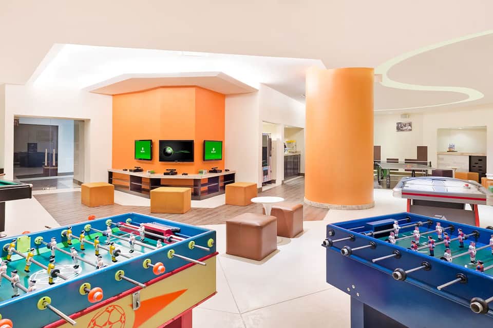 Indoor recreation center with foosball tables and gaming screens with orange accents