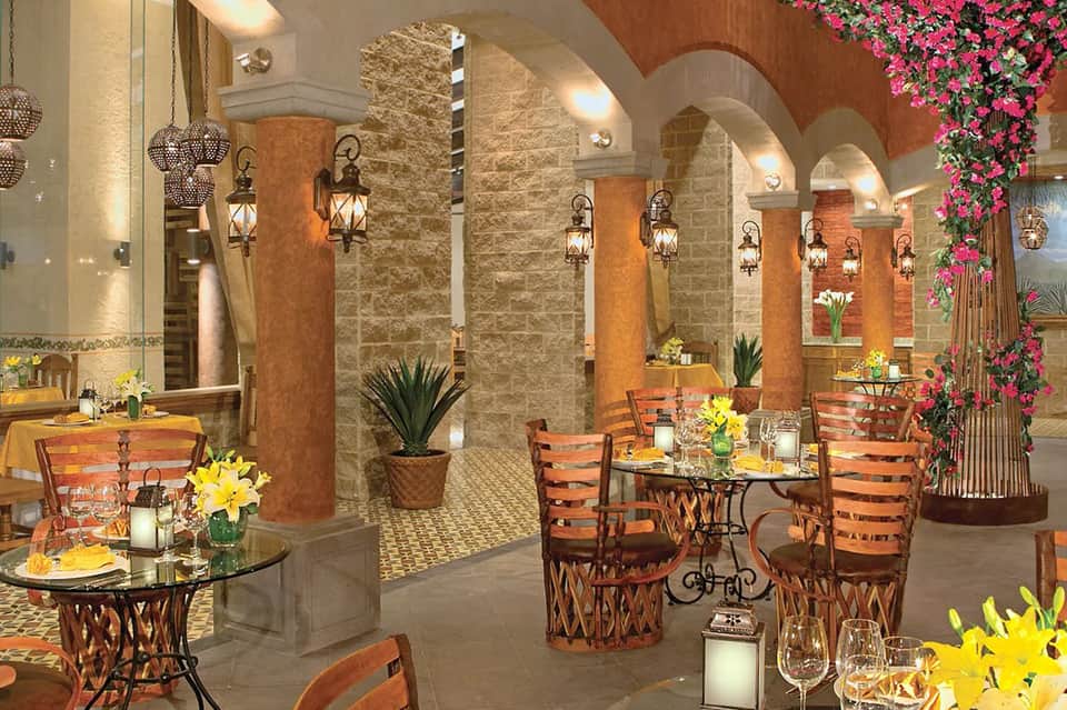 Elegant indoor dining area with arched stone ceilings, hanging lanterns, potted plants, and decorated tables.