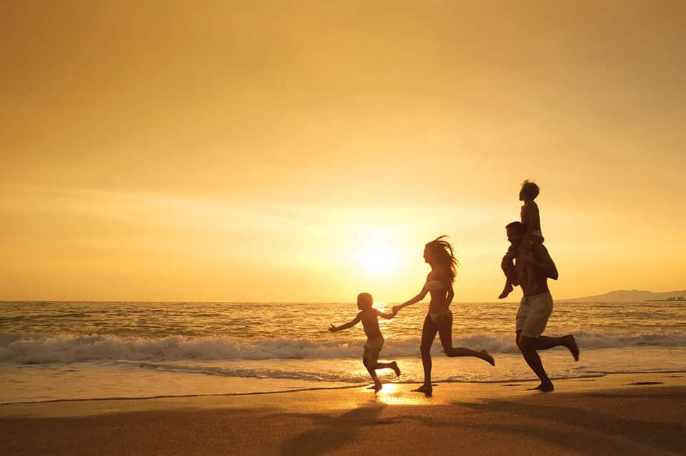Family running on beach at sunset with golden light reflecting on water