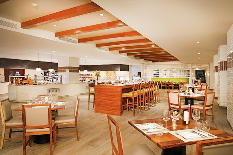 Contemporary open-concept restaurant with wooden beam ceilings, bar seating, and dining tables in warm tones