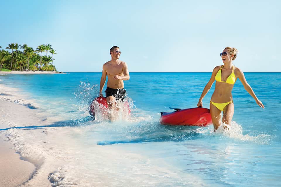 Couple running into clear turquoise ocean waters on white sand beach with palm trees
