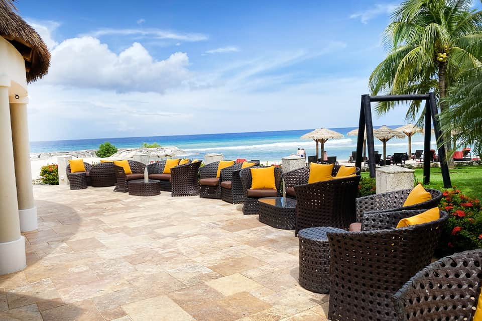 Beachfront resort lounge with dark wicker furniture, yellow cushions, and ocean view