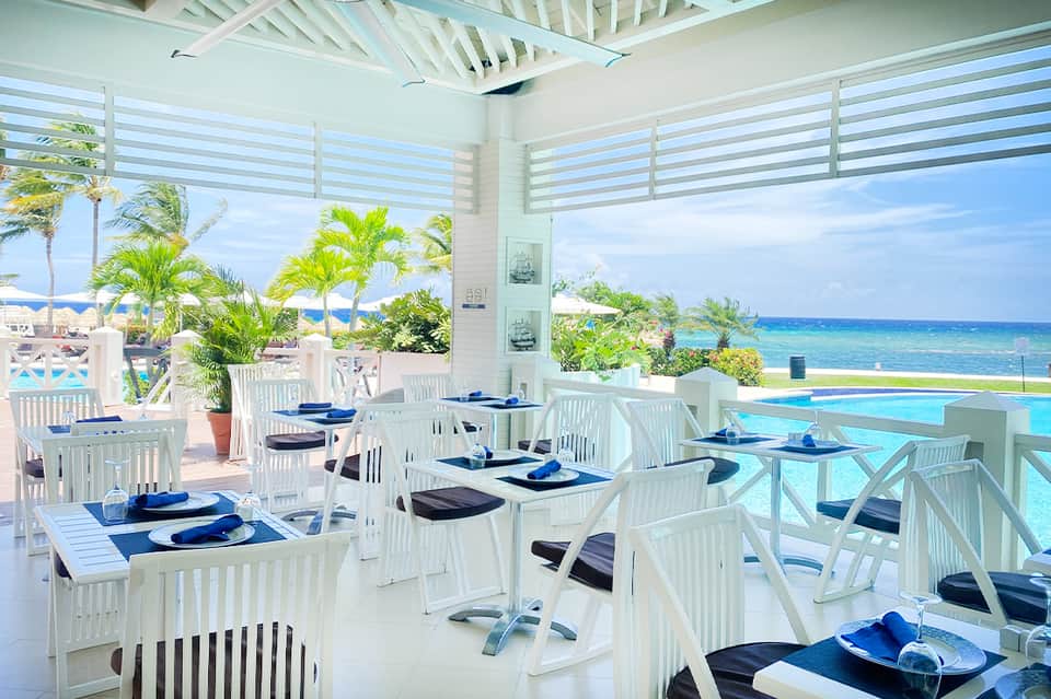 Beachfront restaurant dining area with white furniture, ocean views, and palm trees
