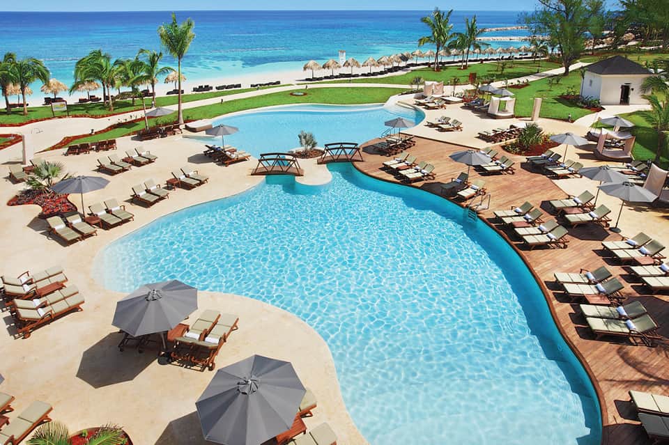 Large curved pool with lounge chairs and ocean beach view