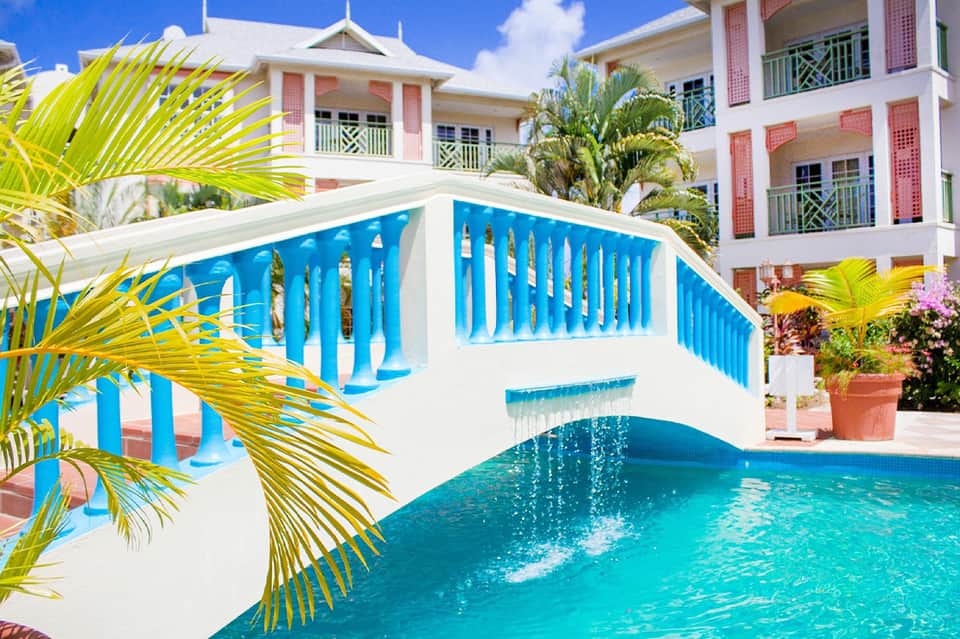 Resort pool with white bridge, palm trees, and colorful Bahamian architecture