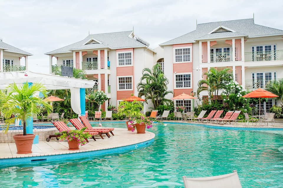 Colorful Caribbean-style resort with coral buildings, pool, and palm trees