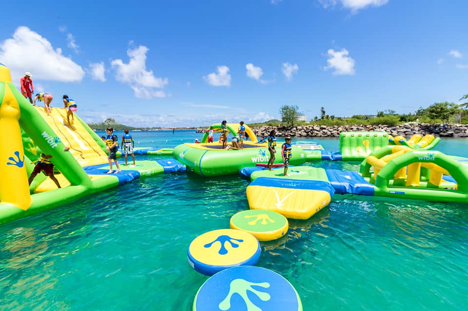 Inflatable water park with green and yellow obstacle course structures in bright turquoise tropical waters