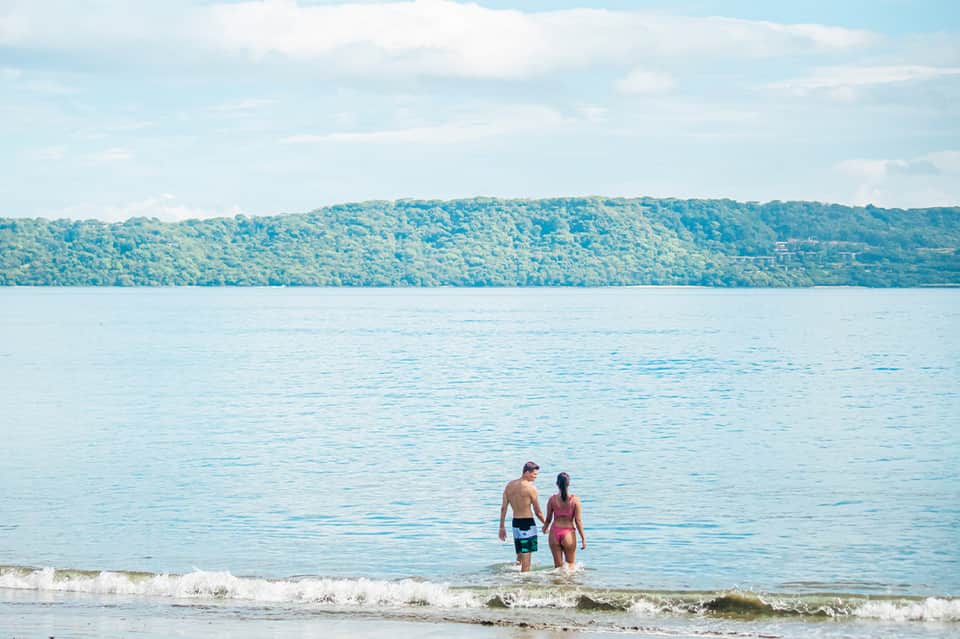 Couple wading in calm turquoise water with forested shoreline and blue sky