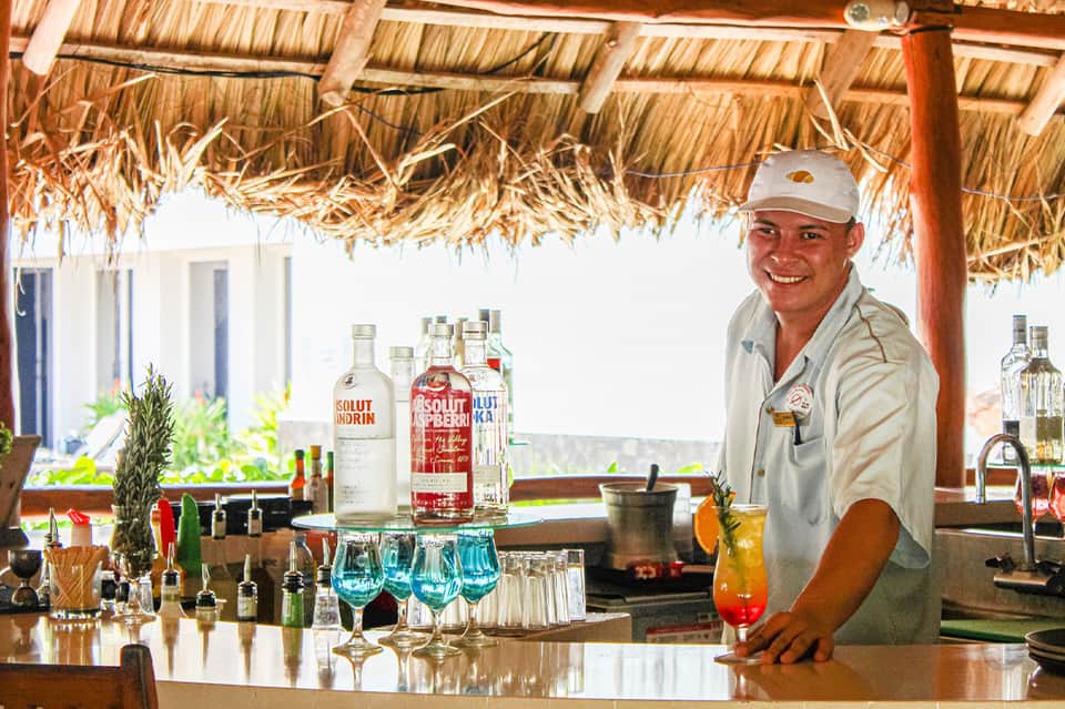 Bartender serving tropical cocktail at beachside bar with thatched roof