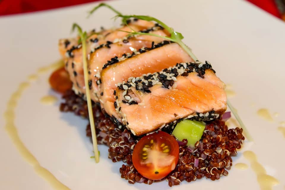 Seared salmon fillet with sesame seeds on red quinoa with tomato and cucumber garnish