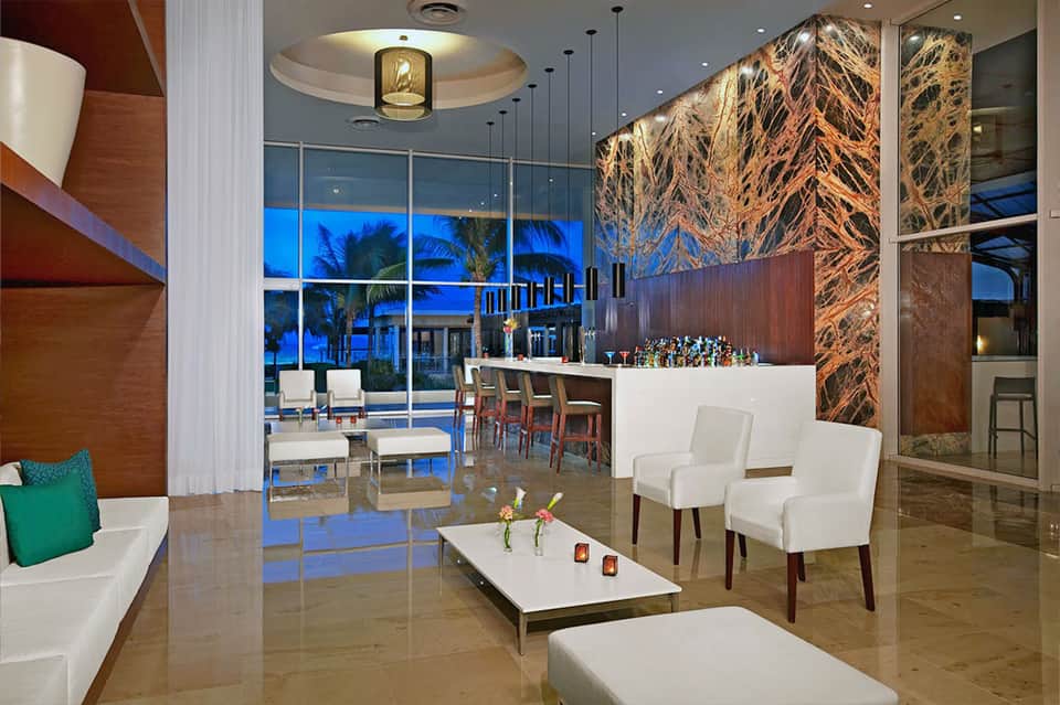 Modern resort lounge with bar, seating, floor-to-ceiling windows, and dusk ocean view