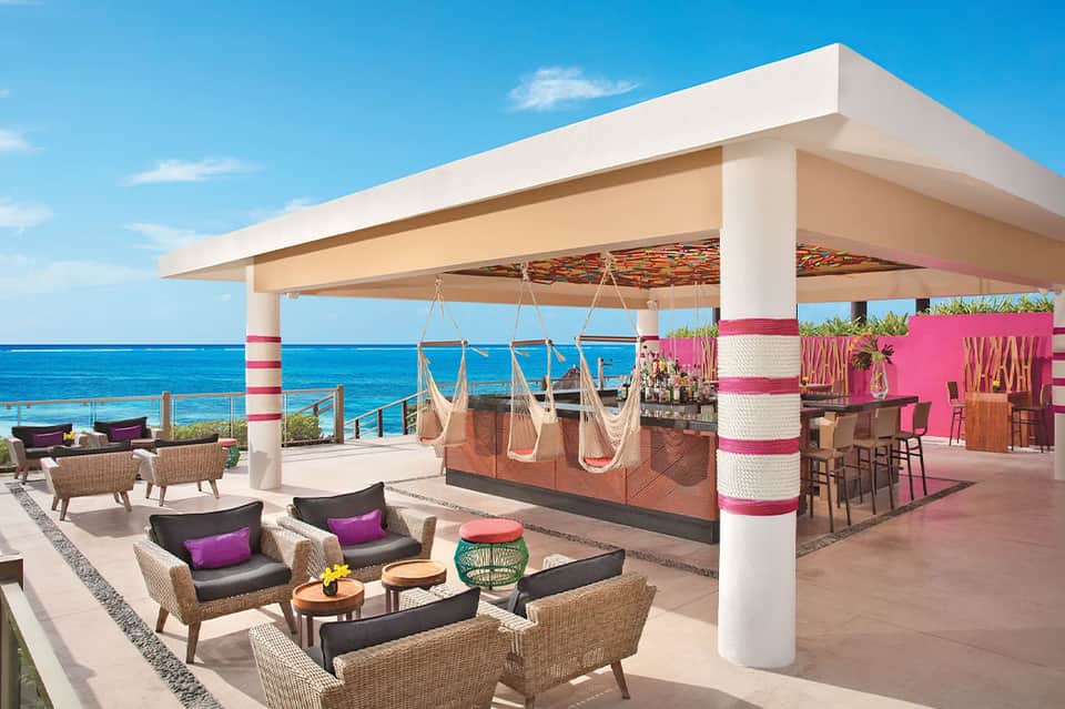 Beachfront resort terrace with white canopy, hammocks, bar area, and ocean views