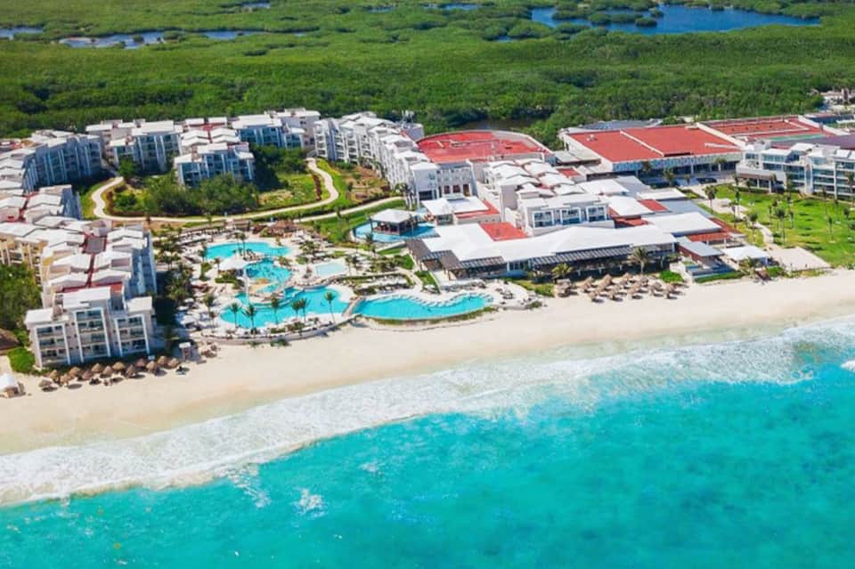 Aerial view of beachfront resort with turquoise pools, sandy beach, and surrounding buildings