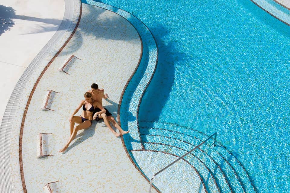 Couple relaxing on lounge chairs at edge of crystalline blue resort pool