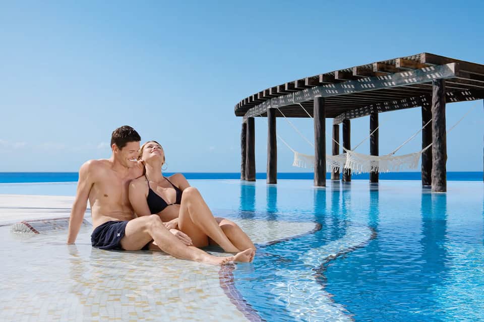 Couple in infinity pool with wooden pergola and ocean horizon backdrop