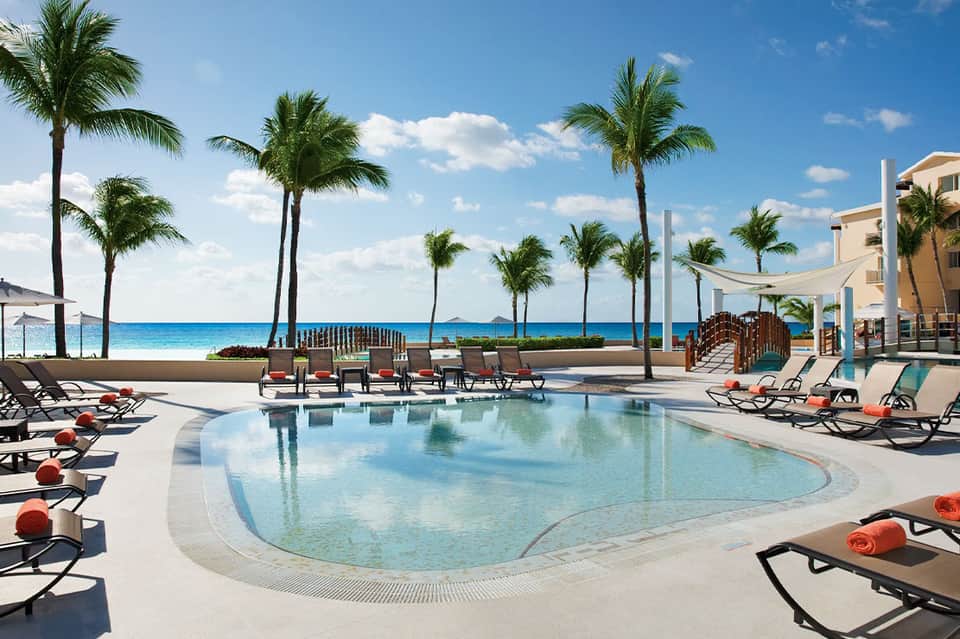 Oceanfront resort pool with palm trees, loungers, and beach views at daytime