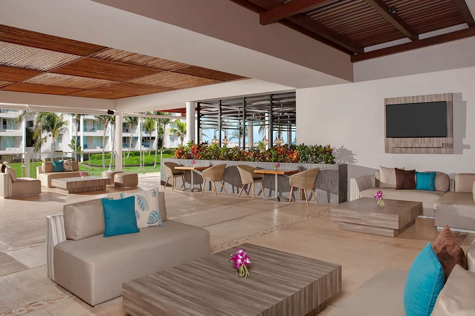 Modern resort lobby with high ceilings, neutral furnishings, ocean view, and tropical landscaping