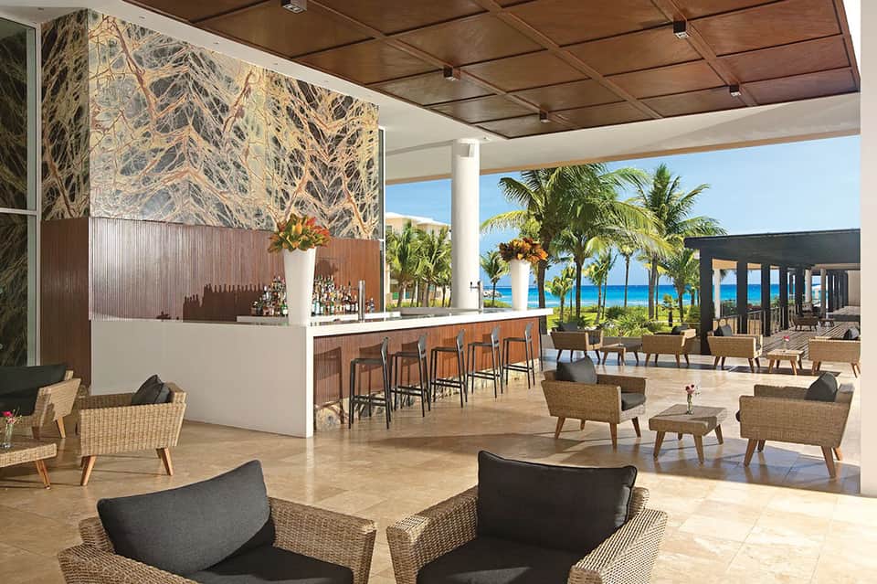 Modern resort bar and lounge with ocean views, wooden elements, wicker seating, and ocean vista