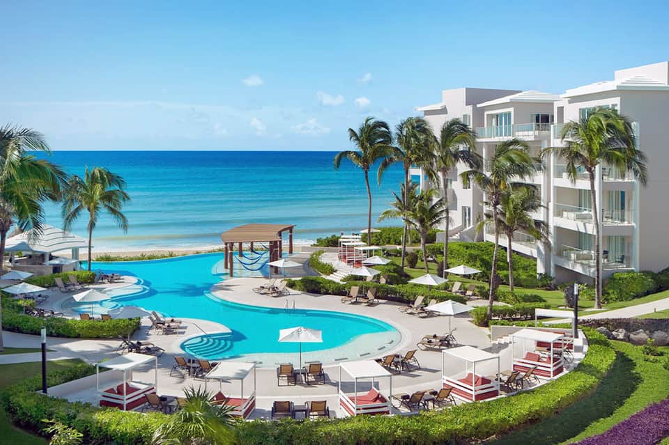 Beachfront resort with curved pool, palm trees, white buildings, and ocean view