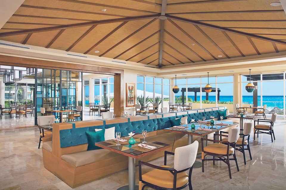 Modern resort dining room with wooden ceiling, turquoise booth seating, ocean views, and contemporary furnishings
