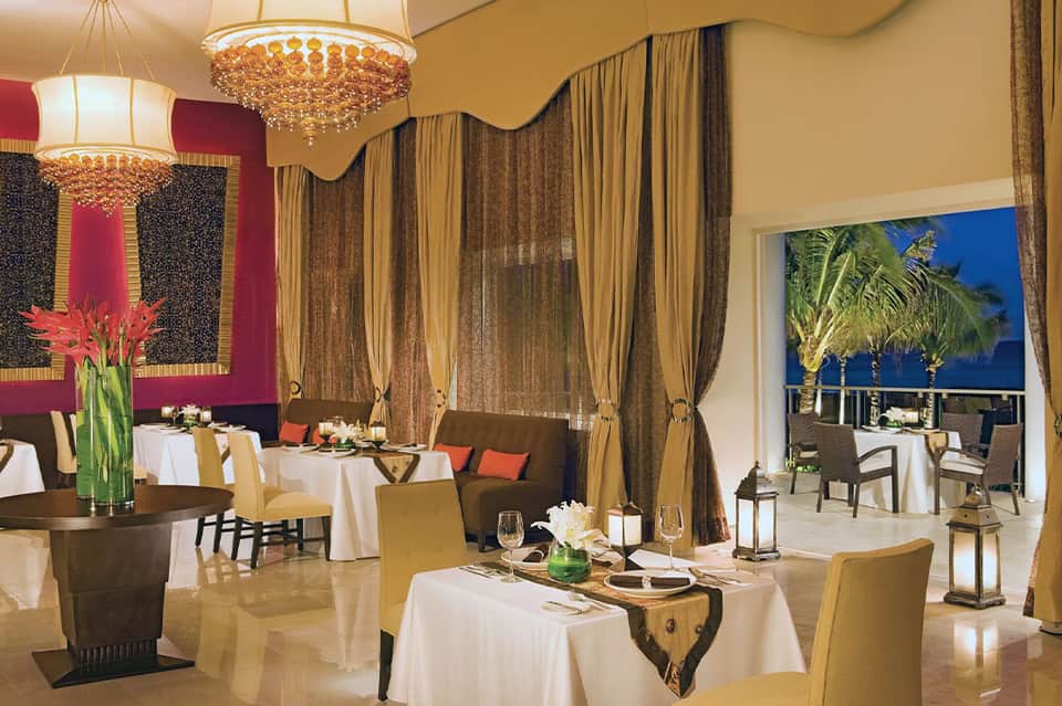Elegant fine dining restaurant with gold chandeliers, draped curtains, and ocean views