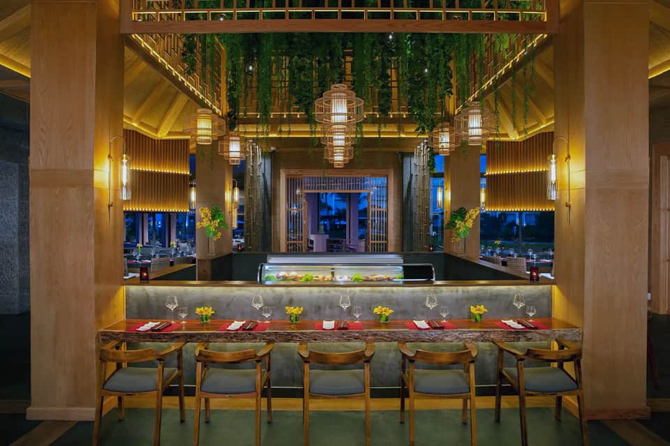 Upscale restaurant bar with wooden ceiling, pendant lights, hanging greenery, and ocean views