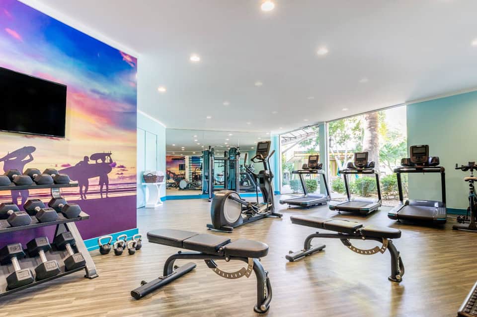 Modern fitness center with colorful wall mural of surfer, treadmills, exercise bikes, and dumbbell weights